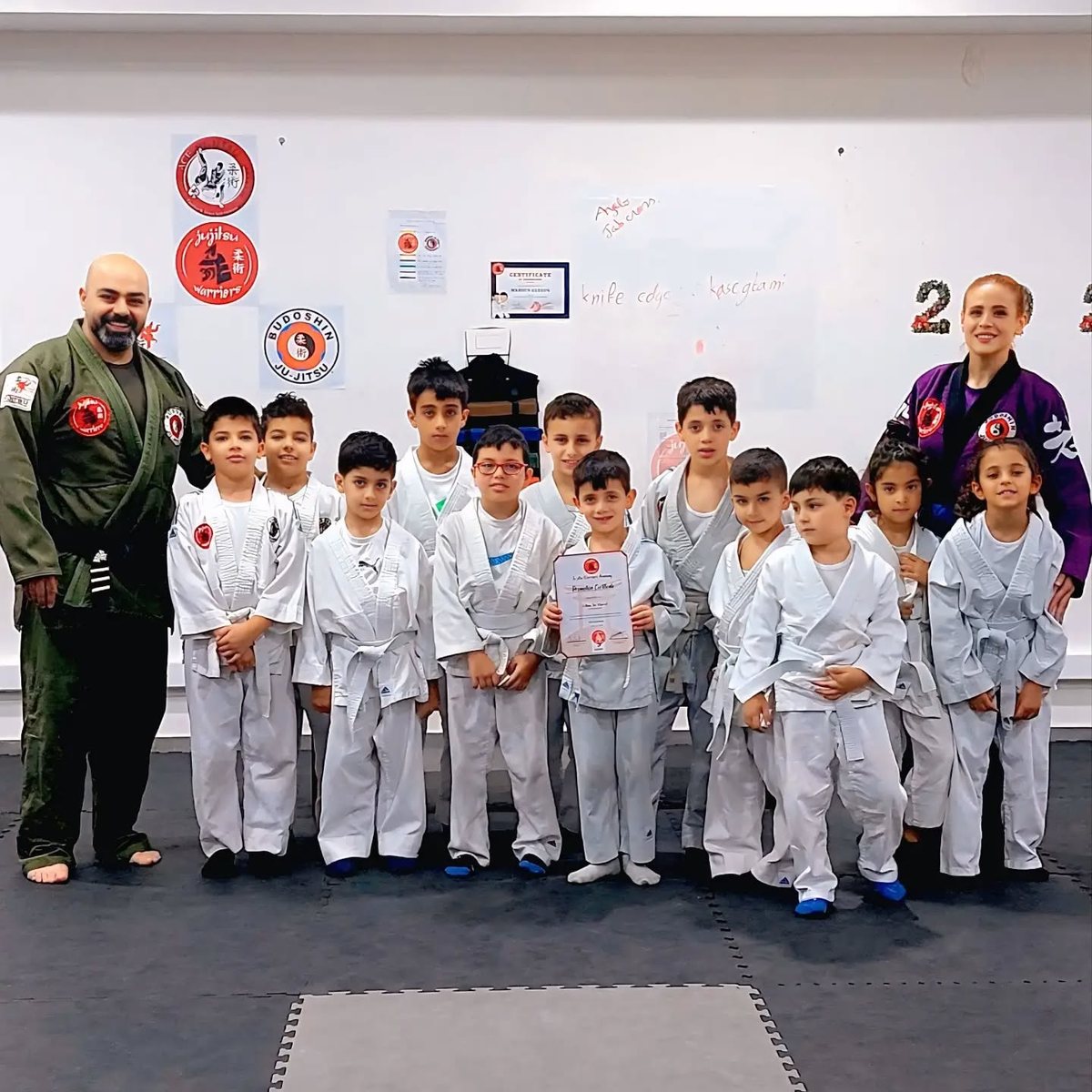 The kids class lined up in white gi with two instructors after a grading