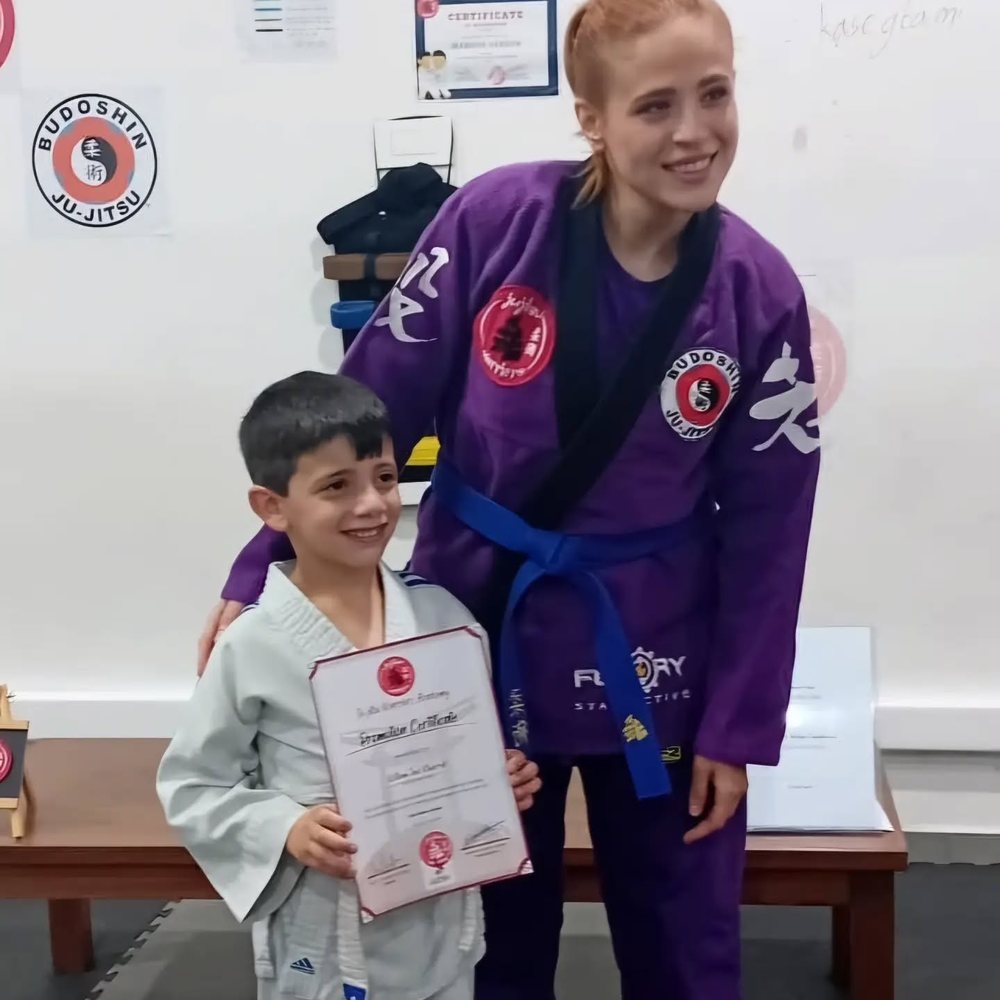 A young student holding his promotion certificate beside his instructor